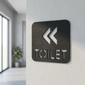 Modern black toilet direction sign with left arrows for offices, cafés and commercial interiors.
