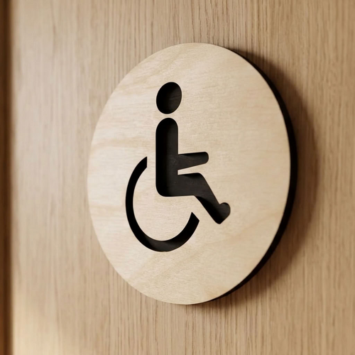 A round light wood handicap sign featuring a black cutout of the wheelchair accessibility symbol, mounted on a matching light wood door.